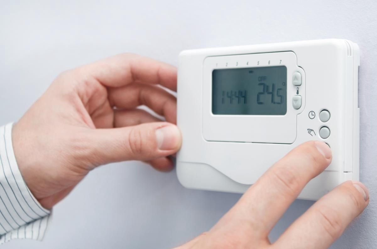 Mano ajustando un termostato de zona en la pared